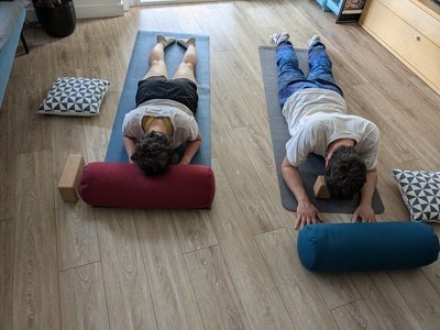 Un groupe de personnes en cours de Yin yoga, utilisant des bolsters pour une posture de flexion avant (sphinx), dans une ambiance de calme et de profonde détente.