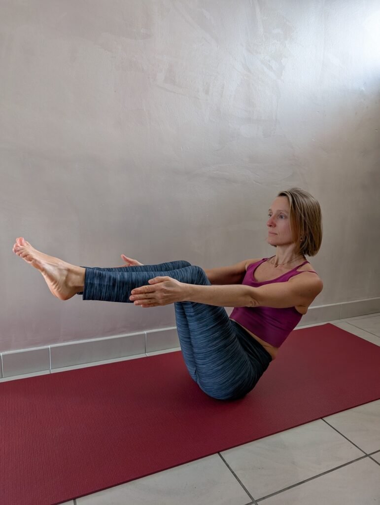 Elise en posture de Navasana, renforçant les abdominaux et l'équilibre, dans un cours de yoga