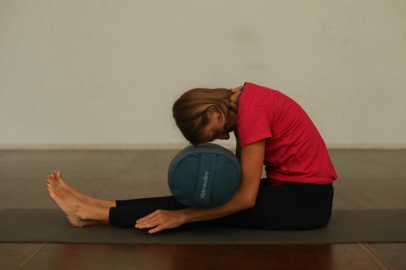 Une personne en posture de flexion avant assise (chenille), utilisant un bolster pour se soutenir, illustrant la détente et le relâchement en Yin yoga.