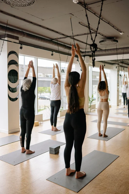 Un groupe de personnes dans un cours de yoga qui pratiquent la posture du volcan (urdhva hasta tadasana).