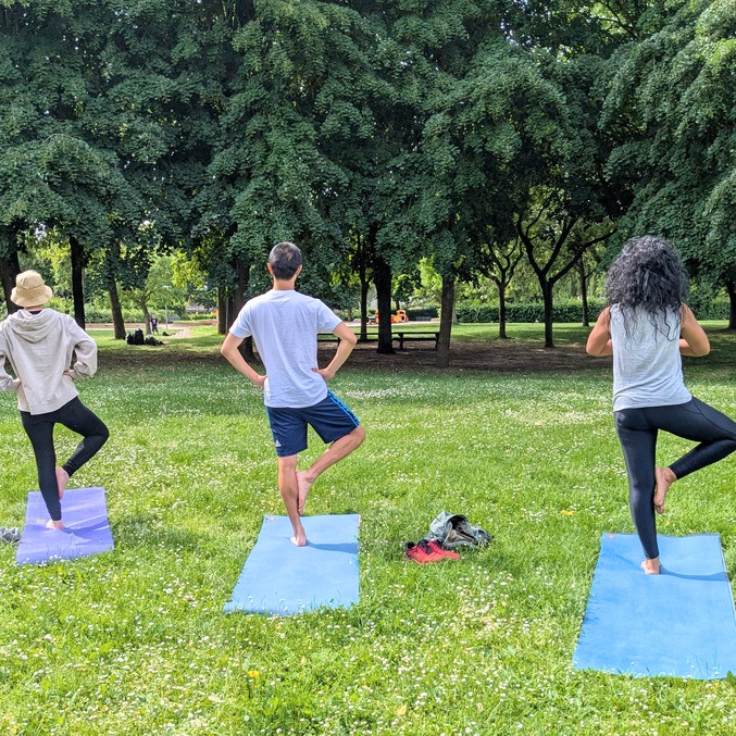 Cours de yoga en plein air dans un parc : deux personnes pratiquant la posture de l'angle étendu (Utthita Parsvakonasana) sur des tapis de yoga.